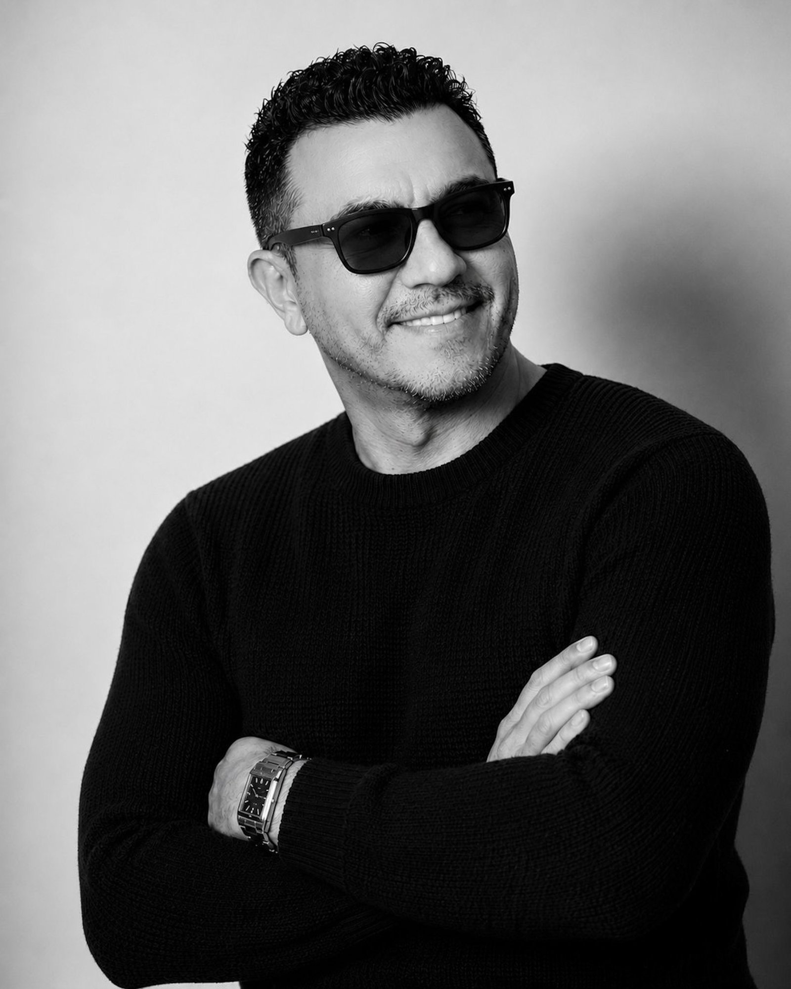 Rafael Castro in a black sweater and sunglasses, smiling in black and white